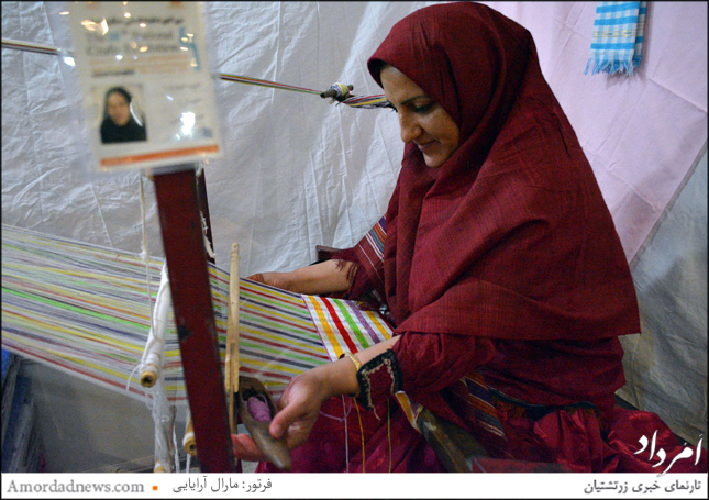  بانویی که از استان سمنان در نمایشگاه شرکت کرده و بافت پارچه‌ها را برای خریداران به نمایش می‌گذارد